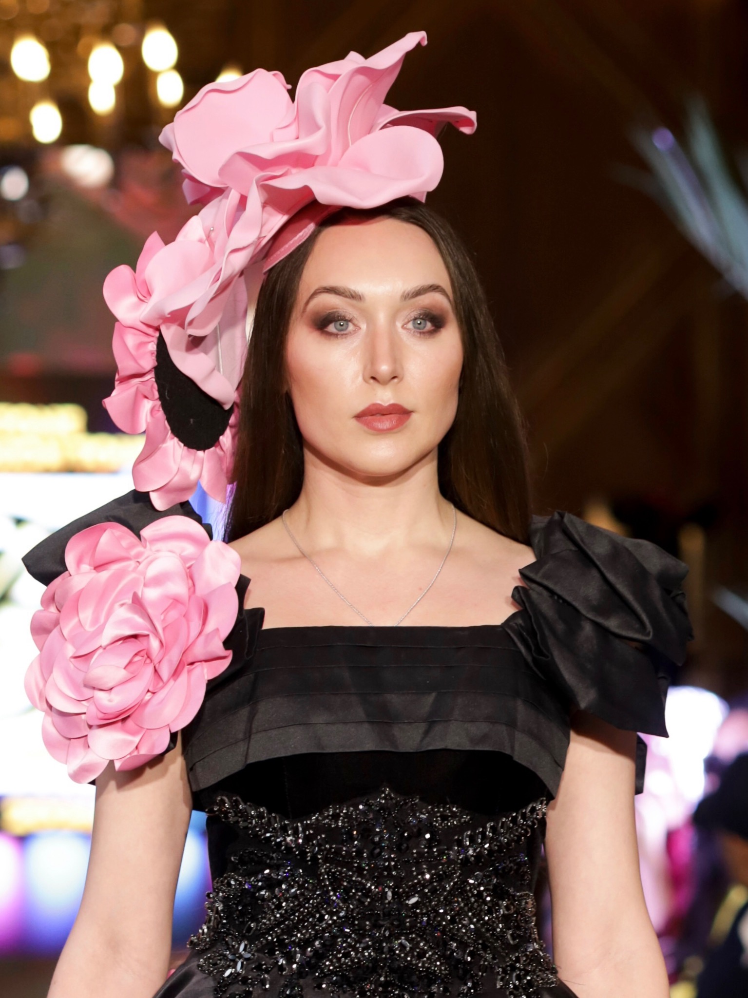 Couture beauty portrait with smoky bronze eyes and a brick-red lip, framed by a pink petal headpiece.