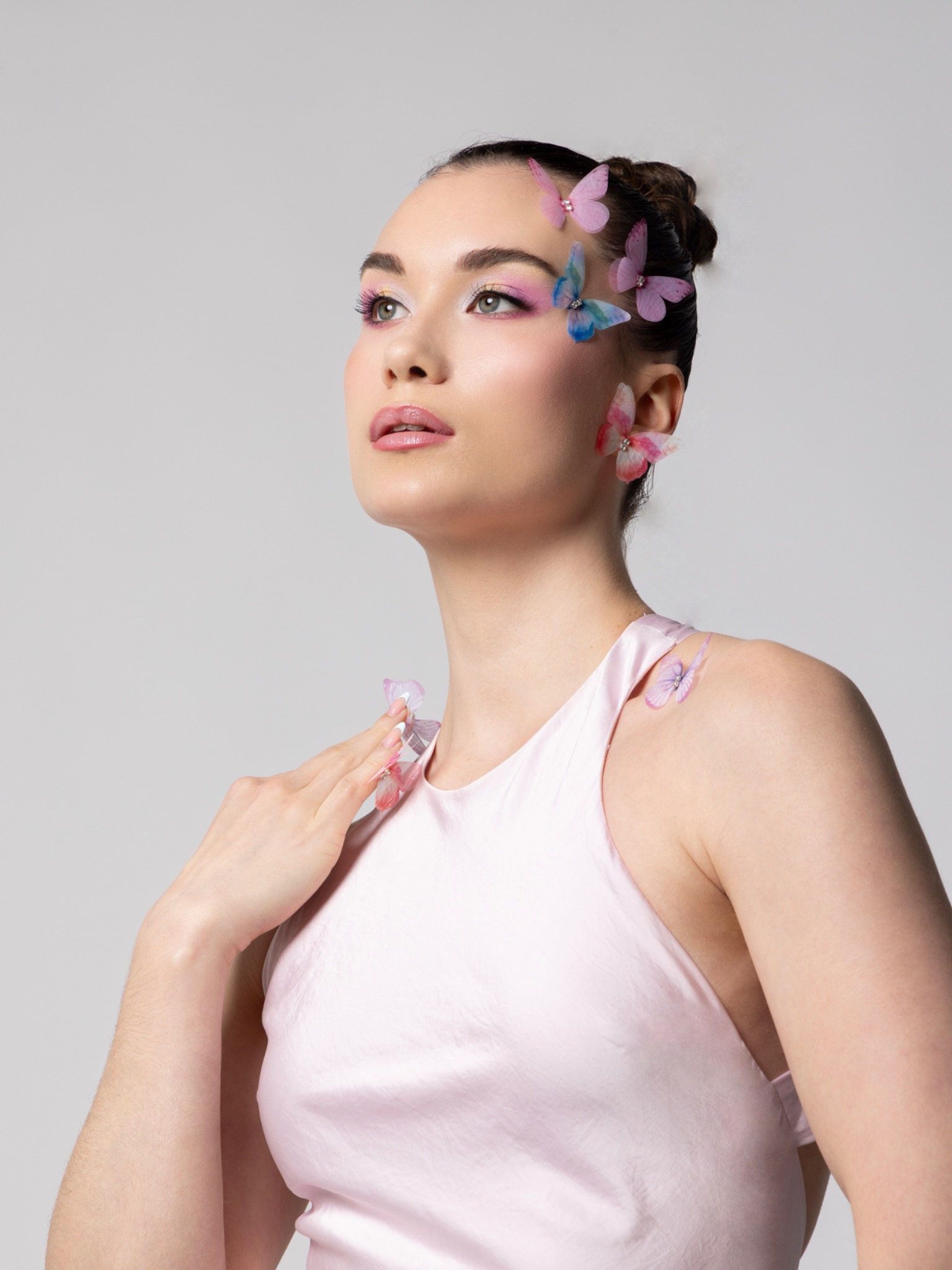 Half-length beauty portrait with pastel pink eye makeup, glowing skin and fabric butterflies in a sleek bun.