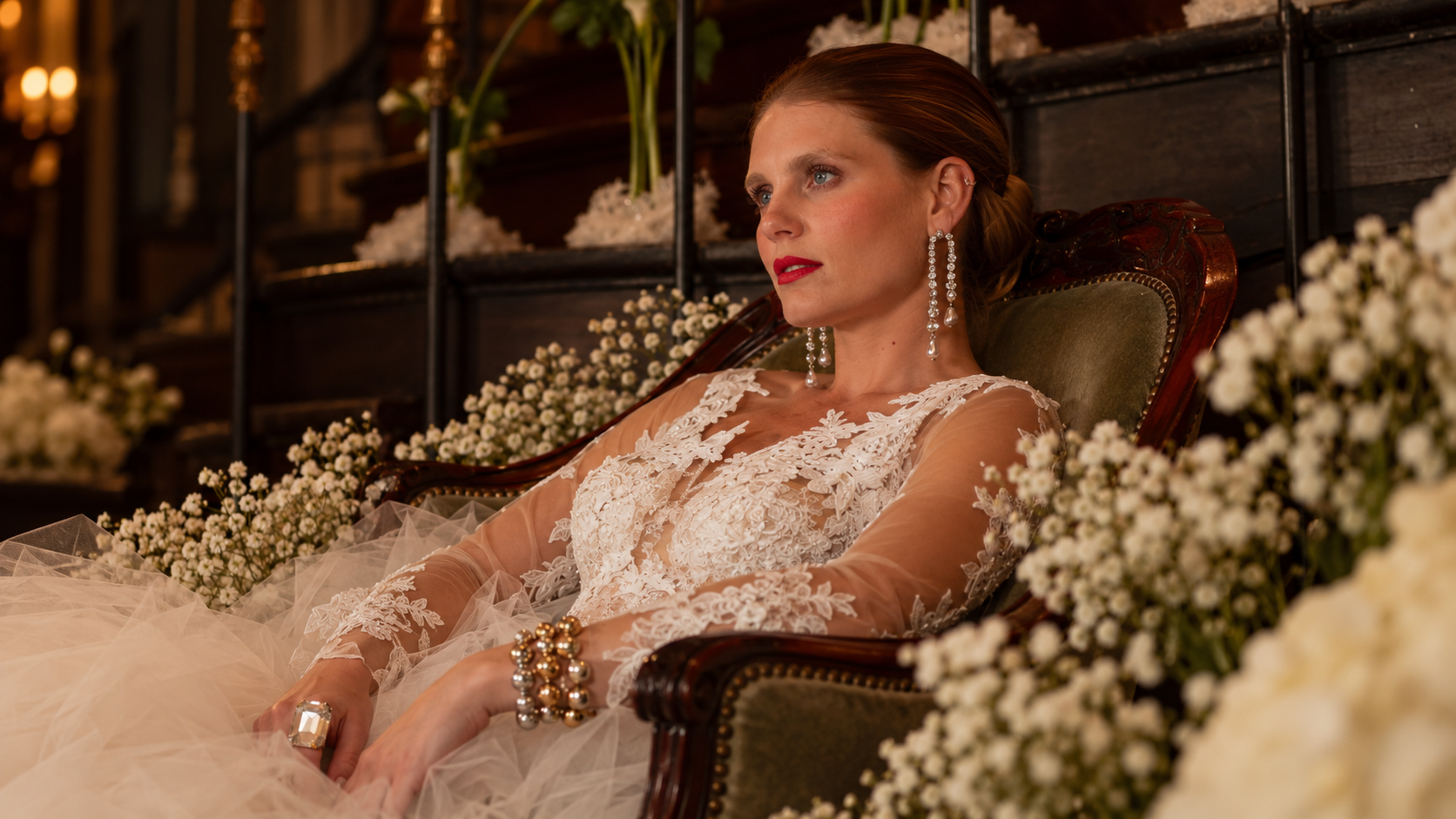 Red-haired bride seated in a flower-filled chair in her wedding dress.