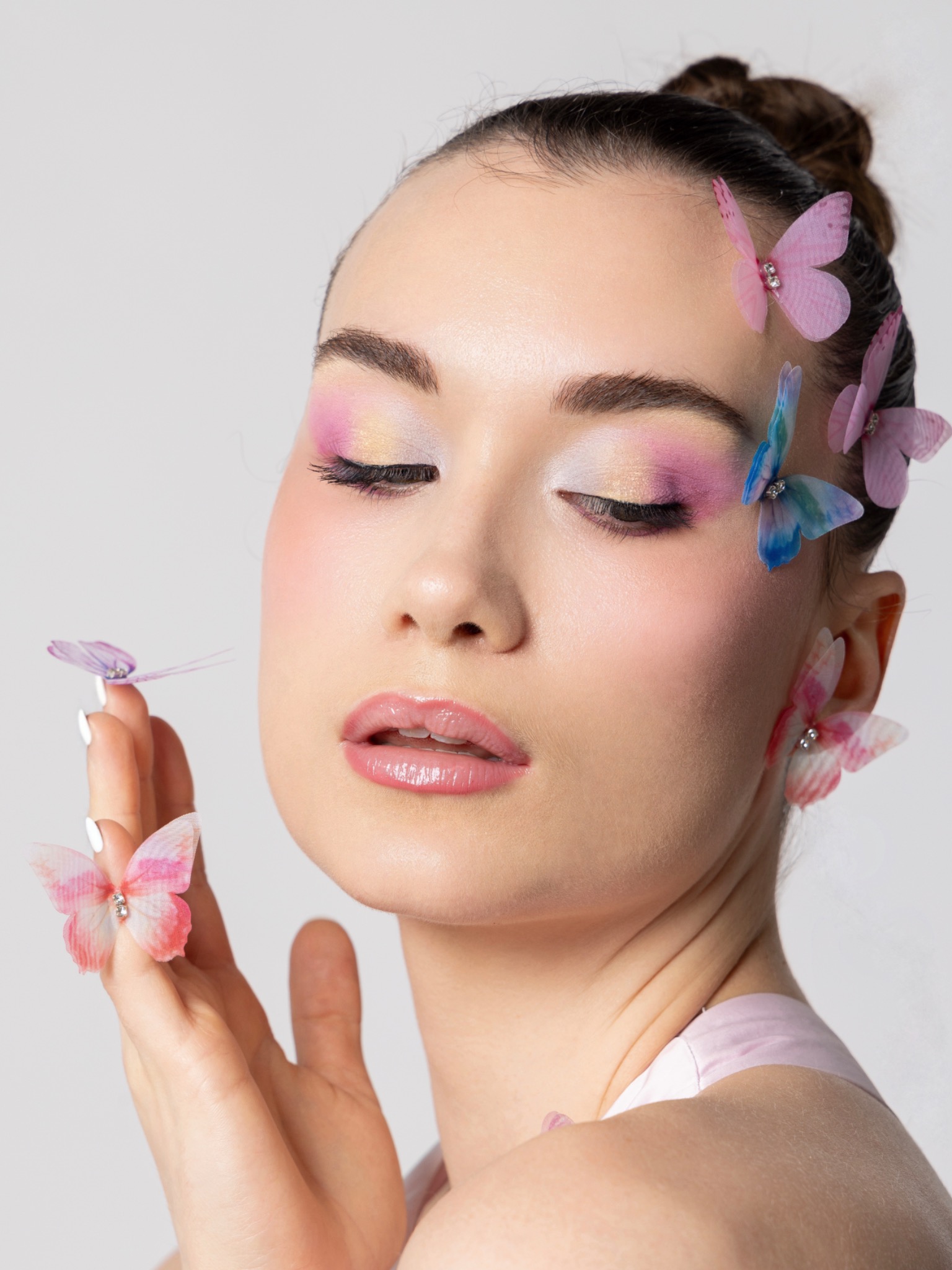 Close beauty portrait with pastel pink and gold shimmer eye makeup, glossy lips and fabric butterflies in the hair.