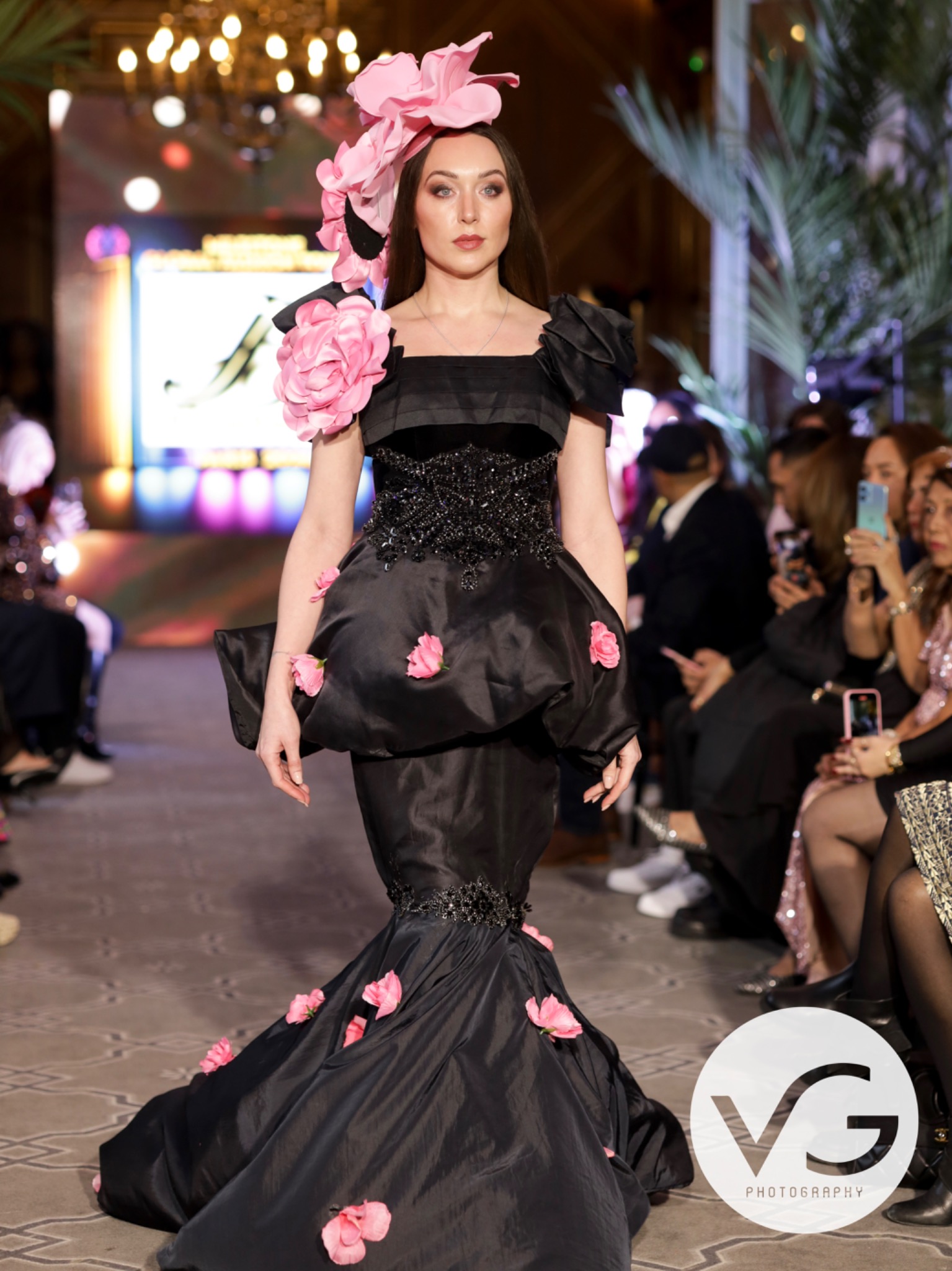 Runway look with warm smoky eyes and matte lip, worn with a black gown and oversized pink floral headpiece.