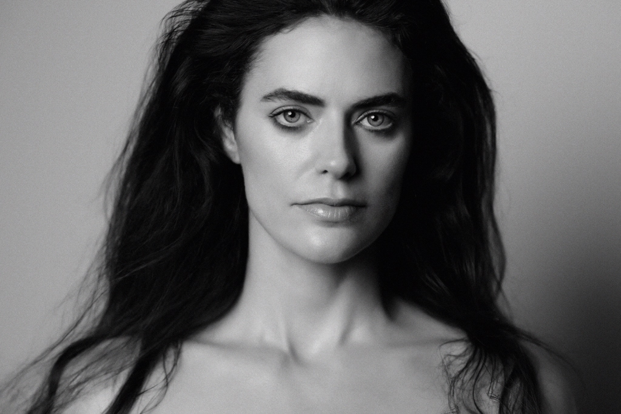 Black and white beauty portrait facing the camera, with polished bare skin, groomed brows and softly defined eyes.