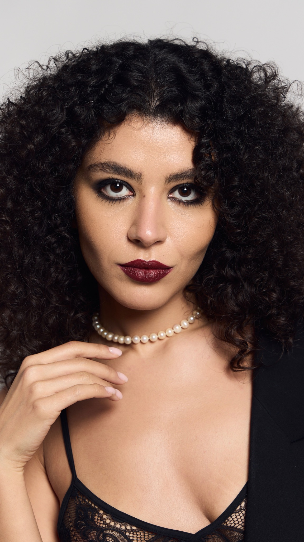 Beauty portrait with smoked grey eyes, defined brows, deep burgundy lips and luminous skin, worn with a pearl necklace.