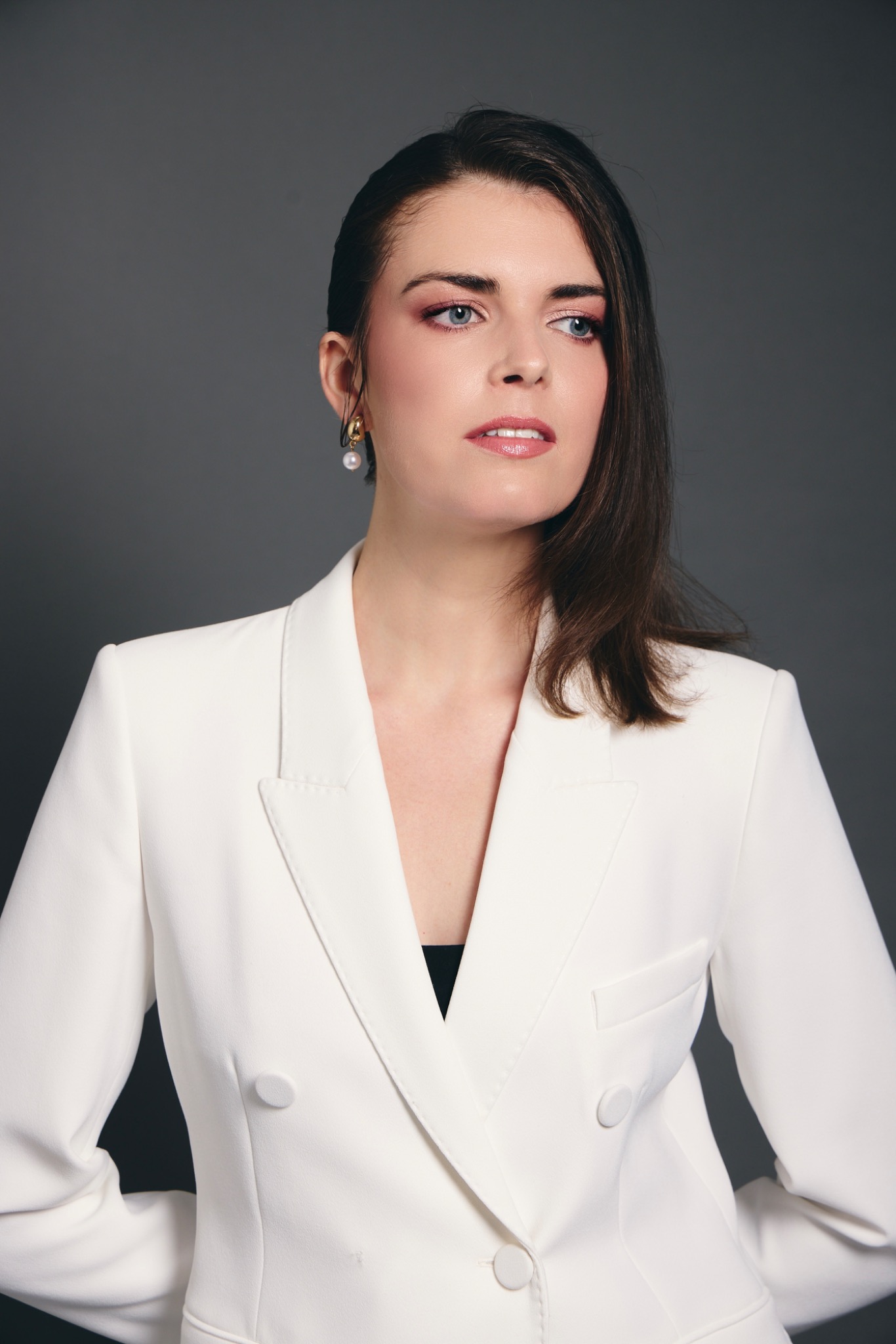 Professional portrait with glowing skin, rose-toned eye shadow, strong brows and a glossy berry lip, in a white tailored jacket.